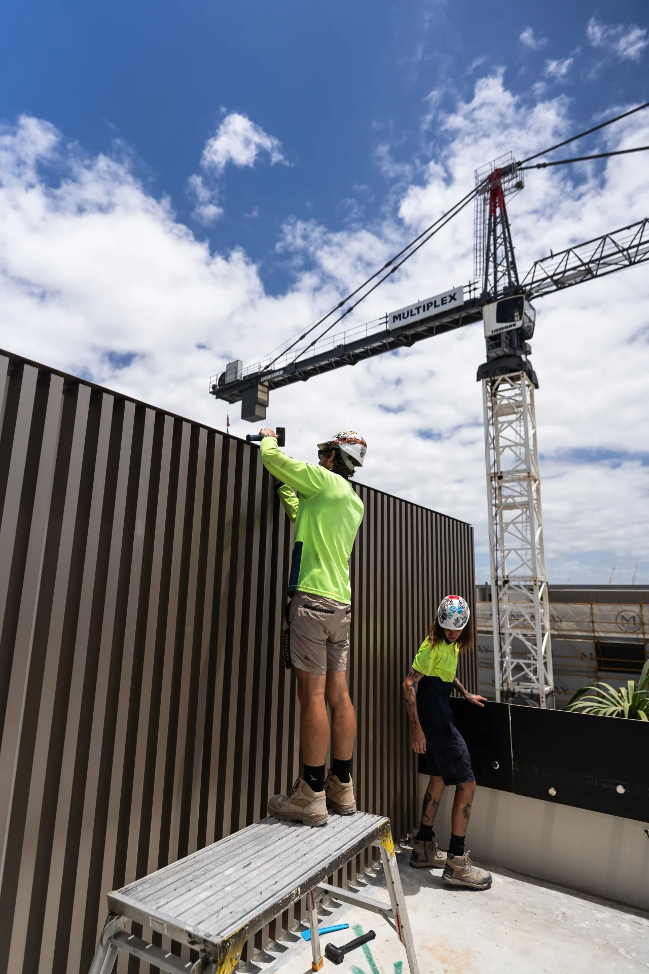 Installer hammering a bronze batten screen into place under the Multiplex crane, Mantaray Main Beach